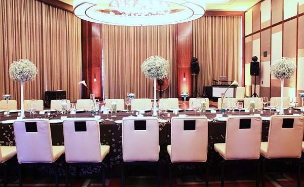 A long table and chairs in a large room with flowers on it.