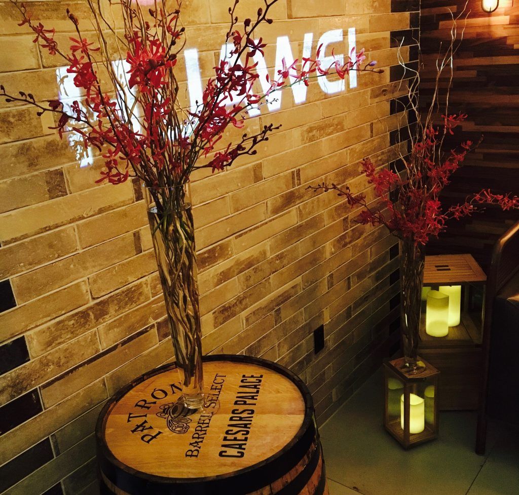 A wooden barrel with a vase of flowers sits in front of a sign that says lunch