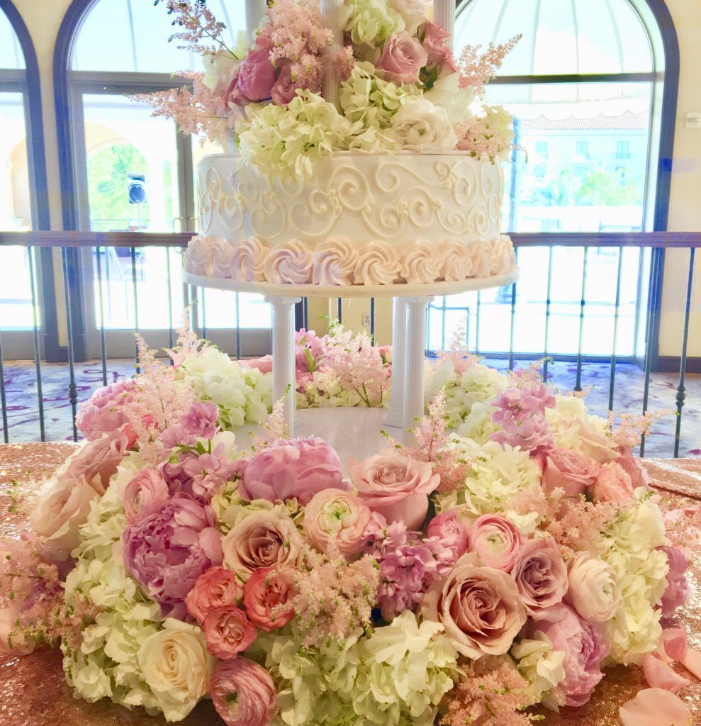 A wedding cake is sitting on top of a table surrounded by pink and white flowers.