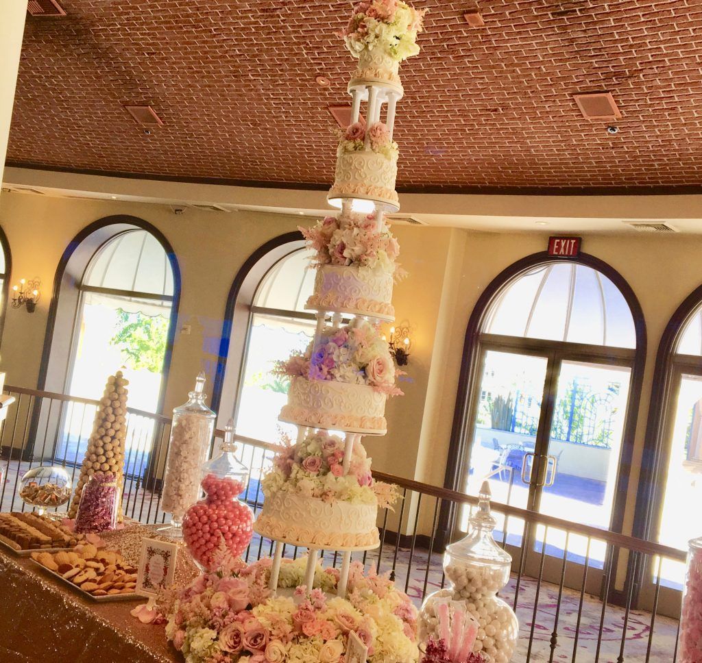 A very tall wedding cake is surrounded by candy and flowers