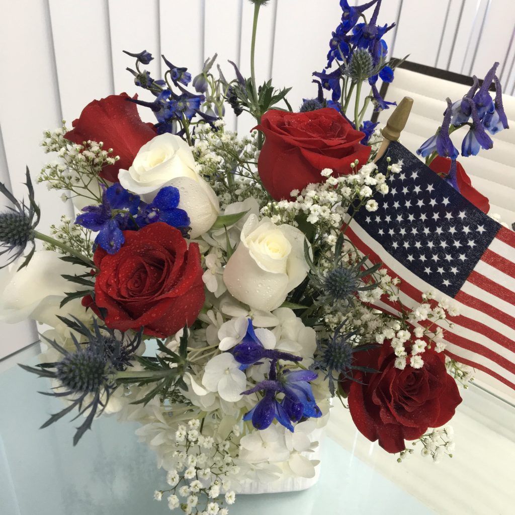 A vase filled with red , white and blue flowers and an american flag.