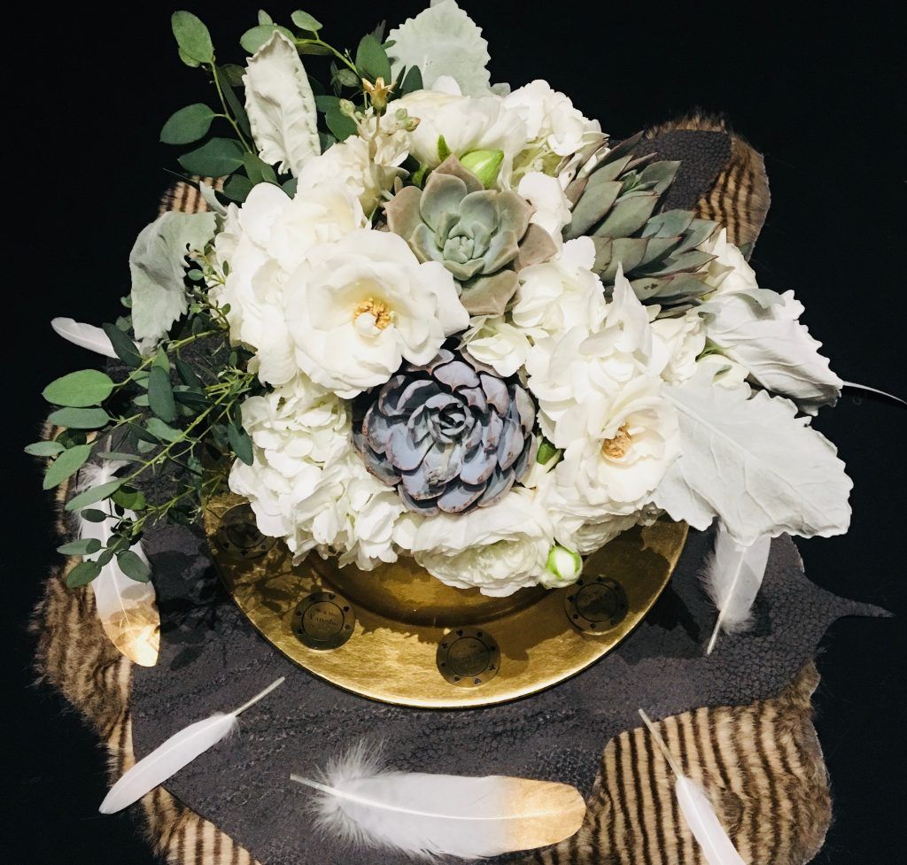 A bouquet of white flowers sits on a table next to feathers