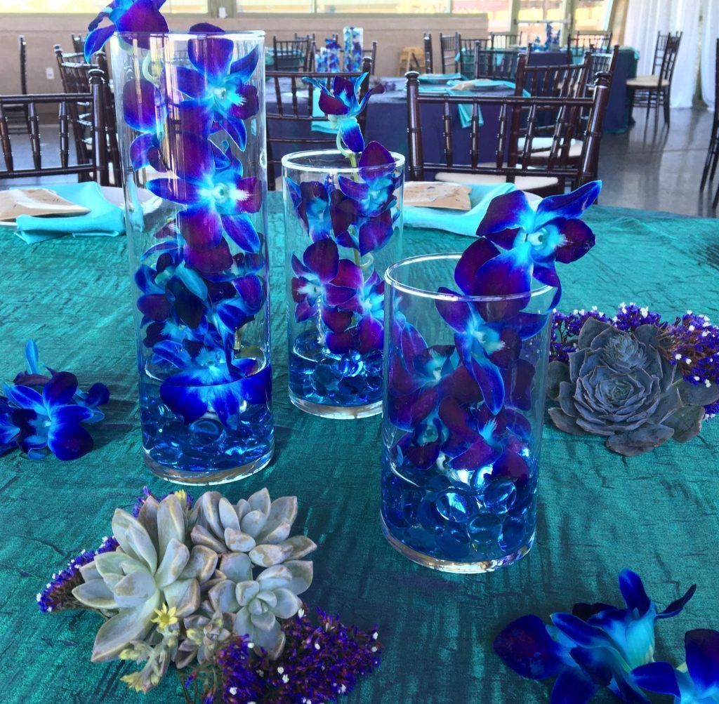Three vases filled with blue and purple flowers are on a table.
