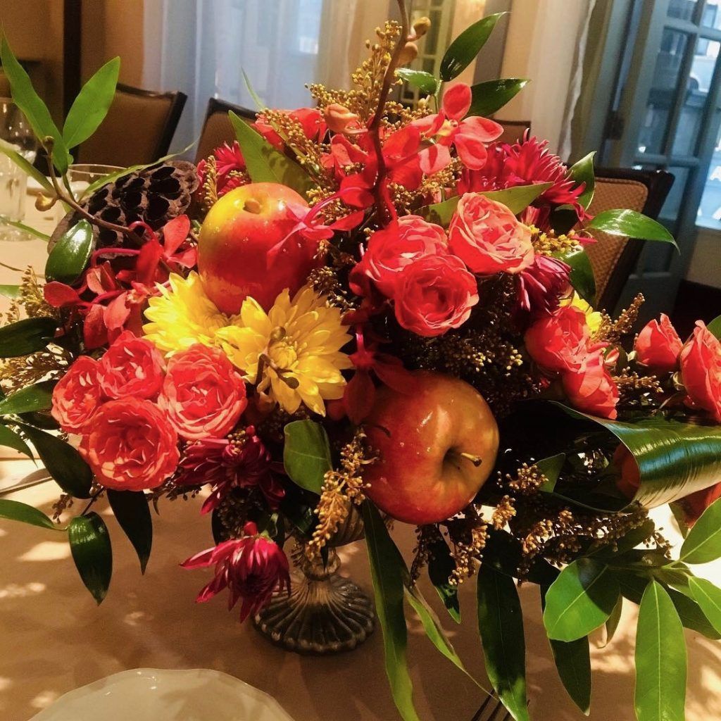 A vase filled with flowers and apples on a table