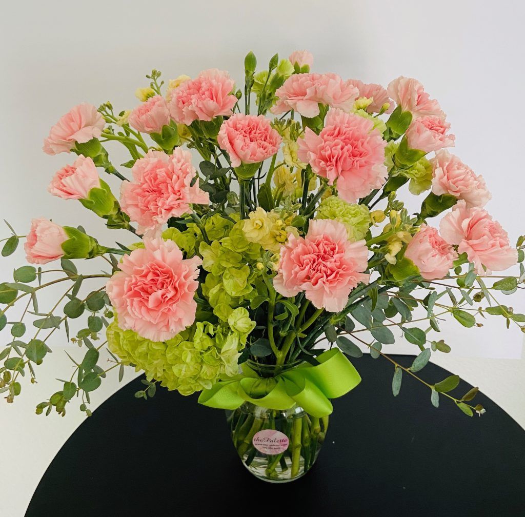 A vase filled with pink carnations and greenery on a table