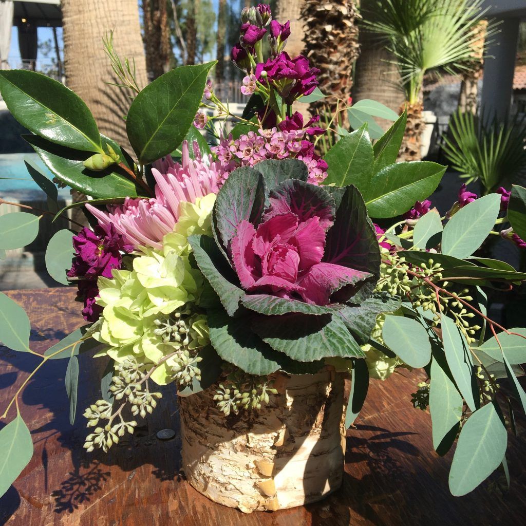A vase filled with flowers and leaves is sitting on a wooden table.