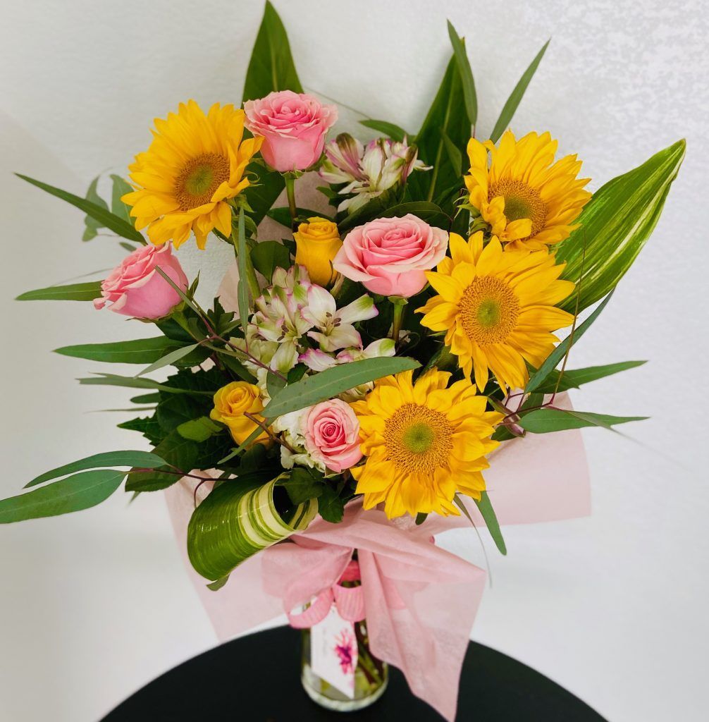 A vase filled with sunflowers and pink roses