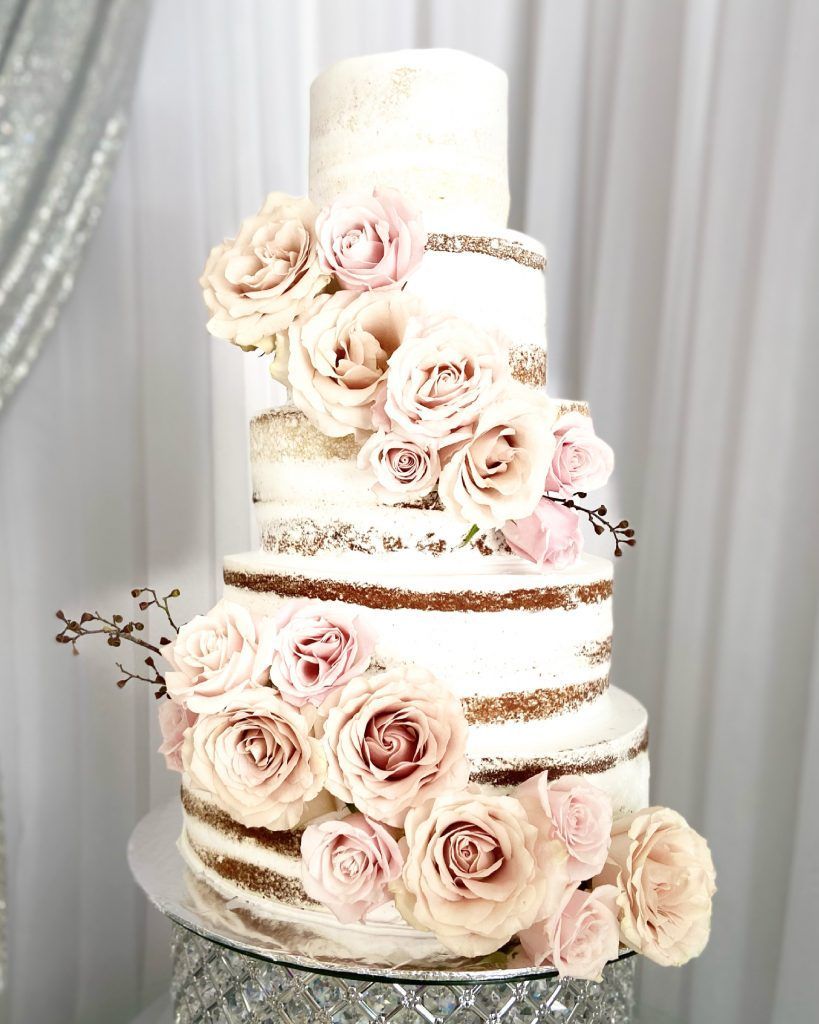 A wedding cake with roses on it is sitting on a table.