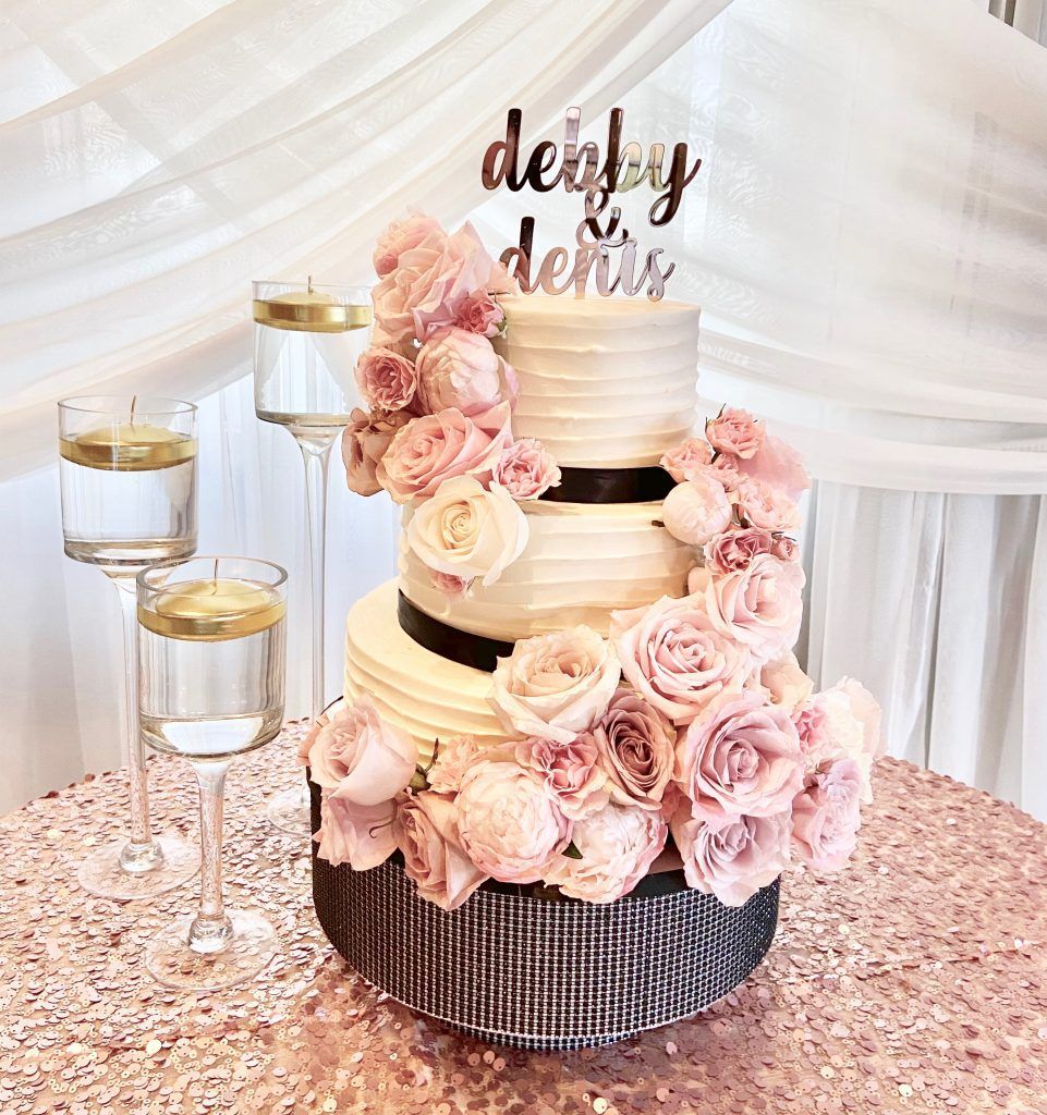 A wedding cake with pink roses and candles on a table.