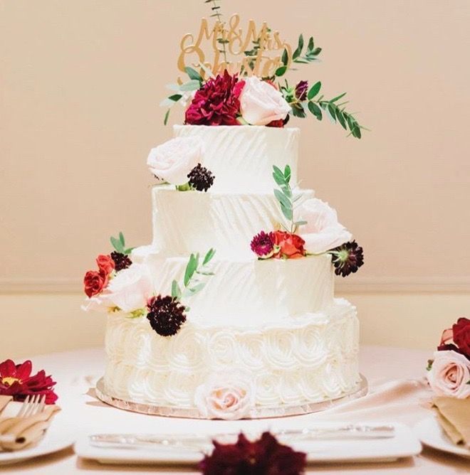 A three tiered wedding cake with flowers and a topper that says mr. and mrs.