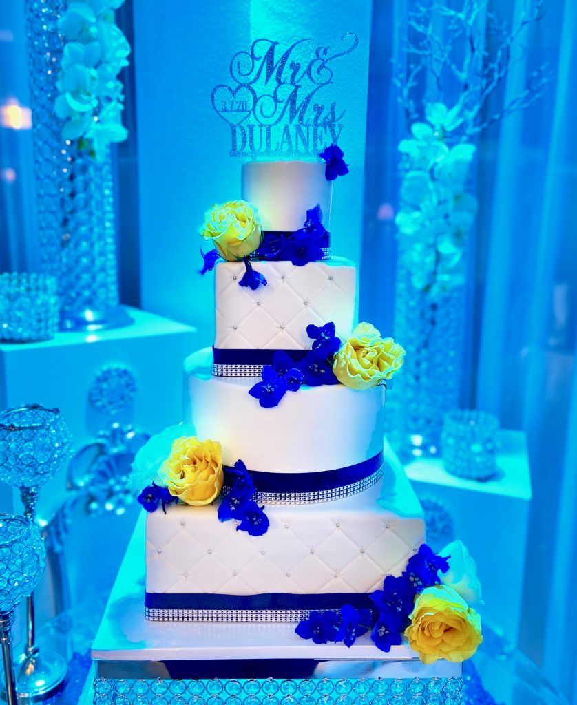 A white wedding cake with blue and yellow flowers is sitting on a table.