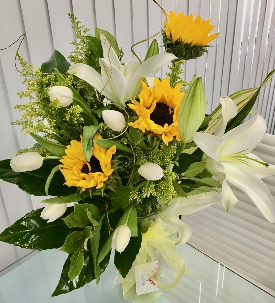 A vase filled with sunflowers and lilies sits on a table