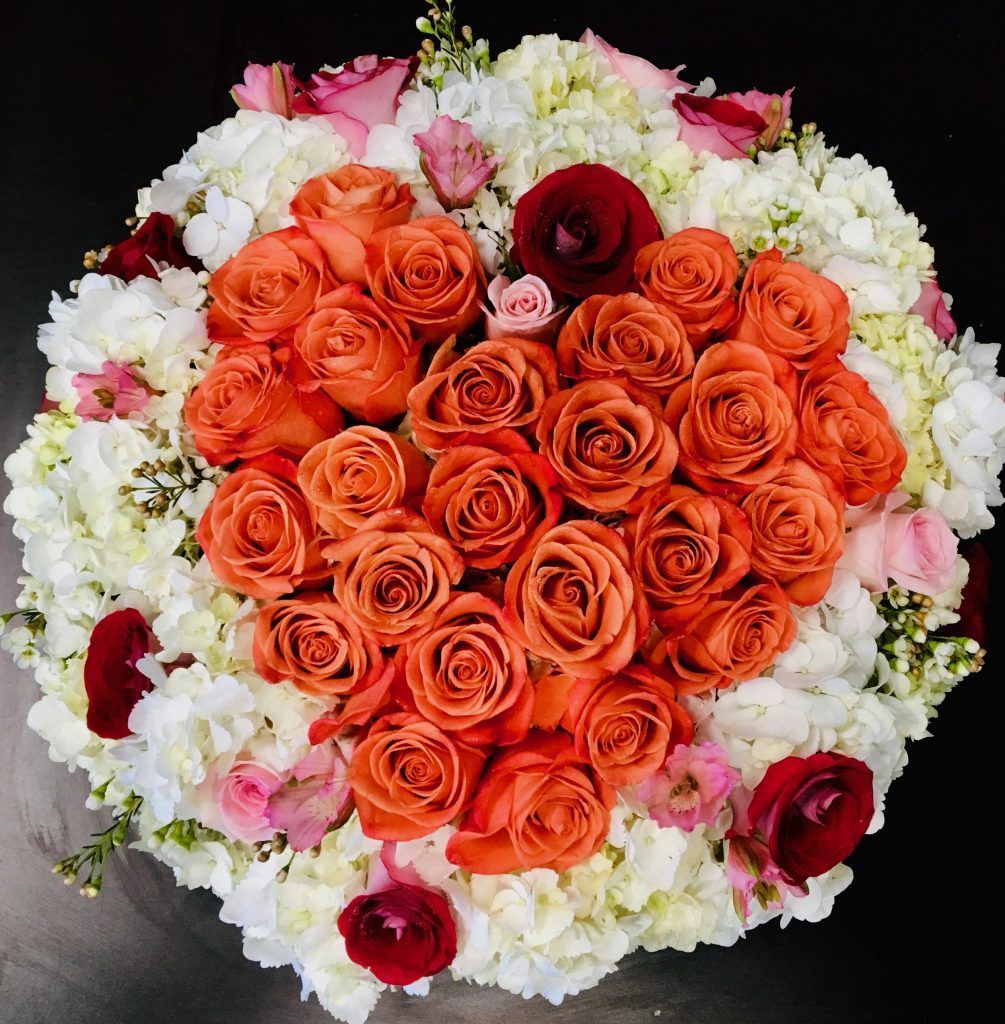 A heart shaped bouquet of orange roses and white flowers