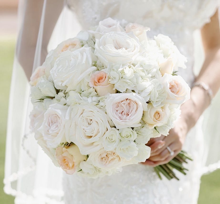 A bride in a white dress is holding a bouquet of white flowers.