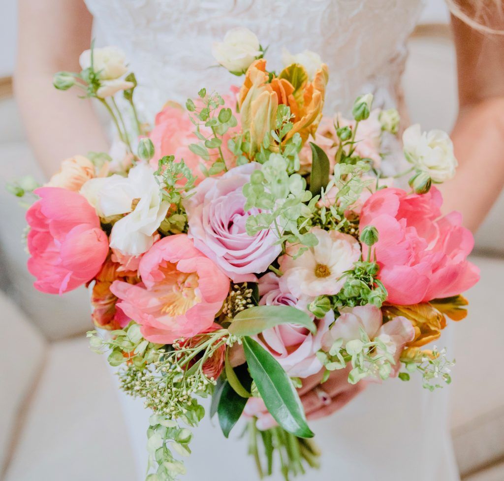 A bride in a white dress is holding a bouquet of pink and white flowers.