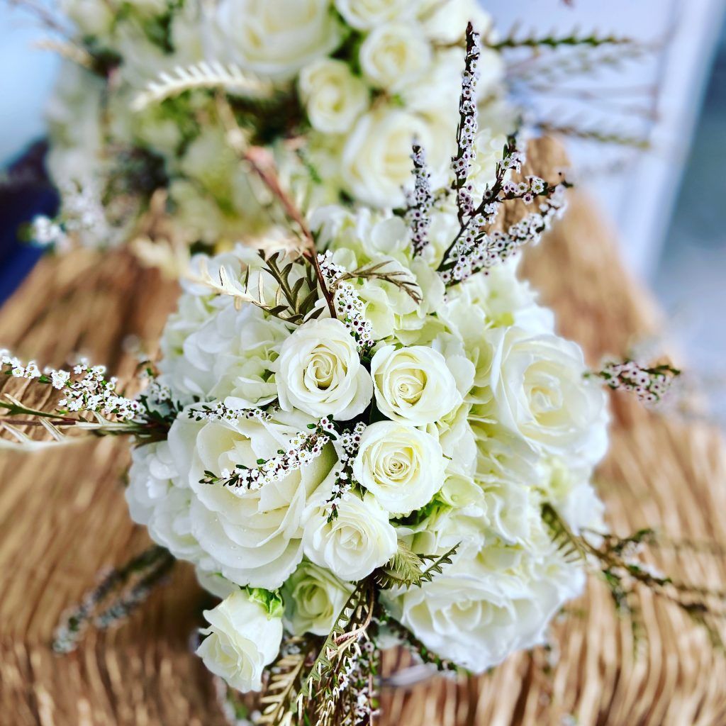 Two bouquets of white roses are sitting on a wooden table.