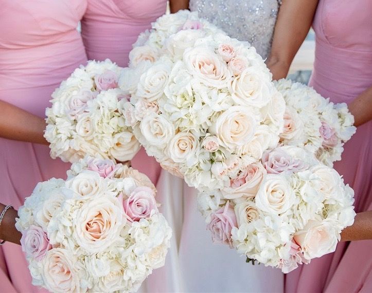 The bride and her bridesmaids are wearing pink dresses and holding bouquets of white flowers.