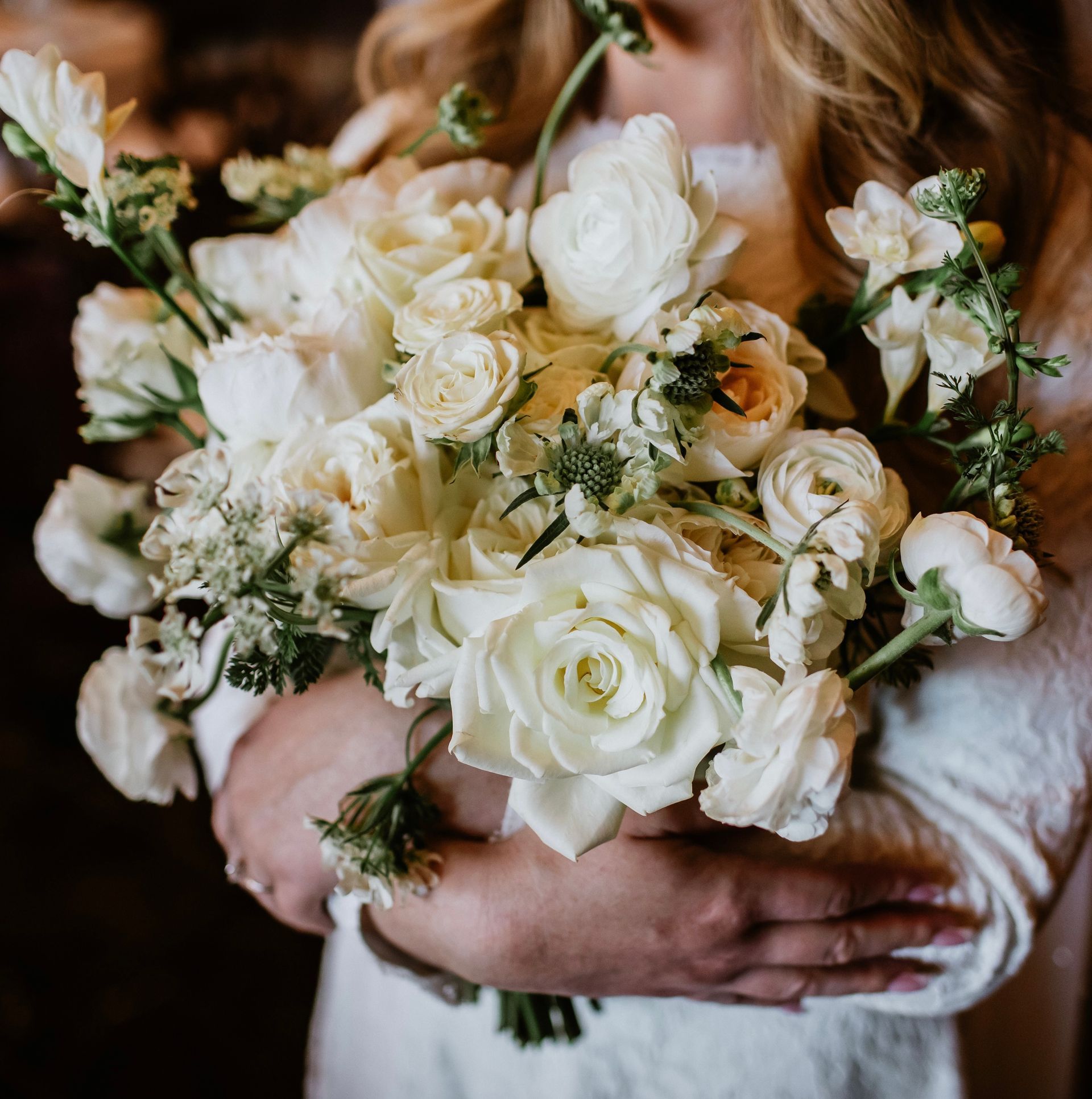 A woman in a white dress is holding a bouquet of white flowers.