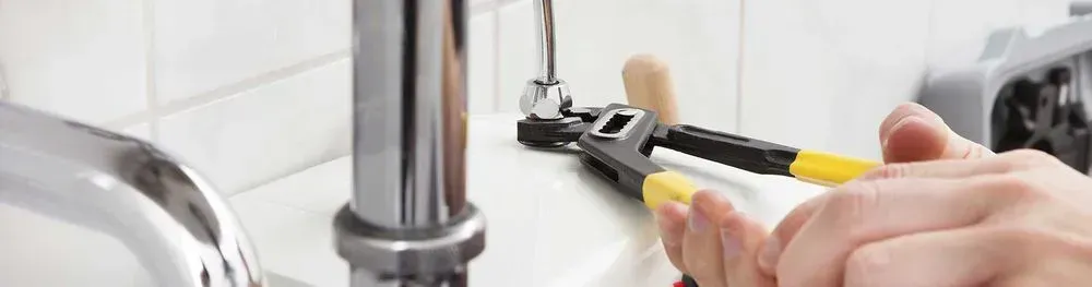 A person is fixing a sink with a wrench and pliers.
