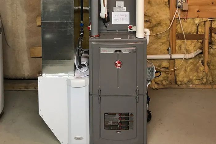 A gray Rheem furnace in a basement setting with ductwork and exposed insulation.