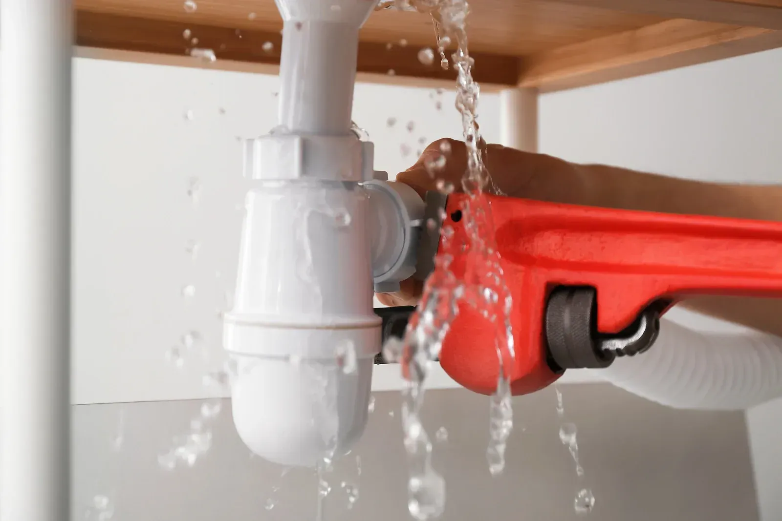 A person is fixing a leaking sink pipe with a wrench.