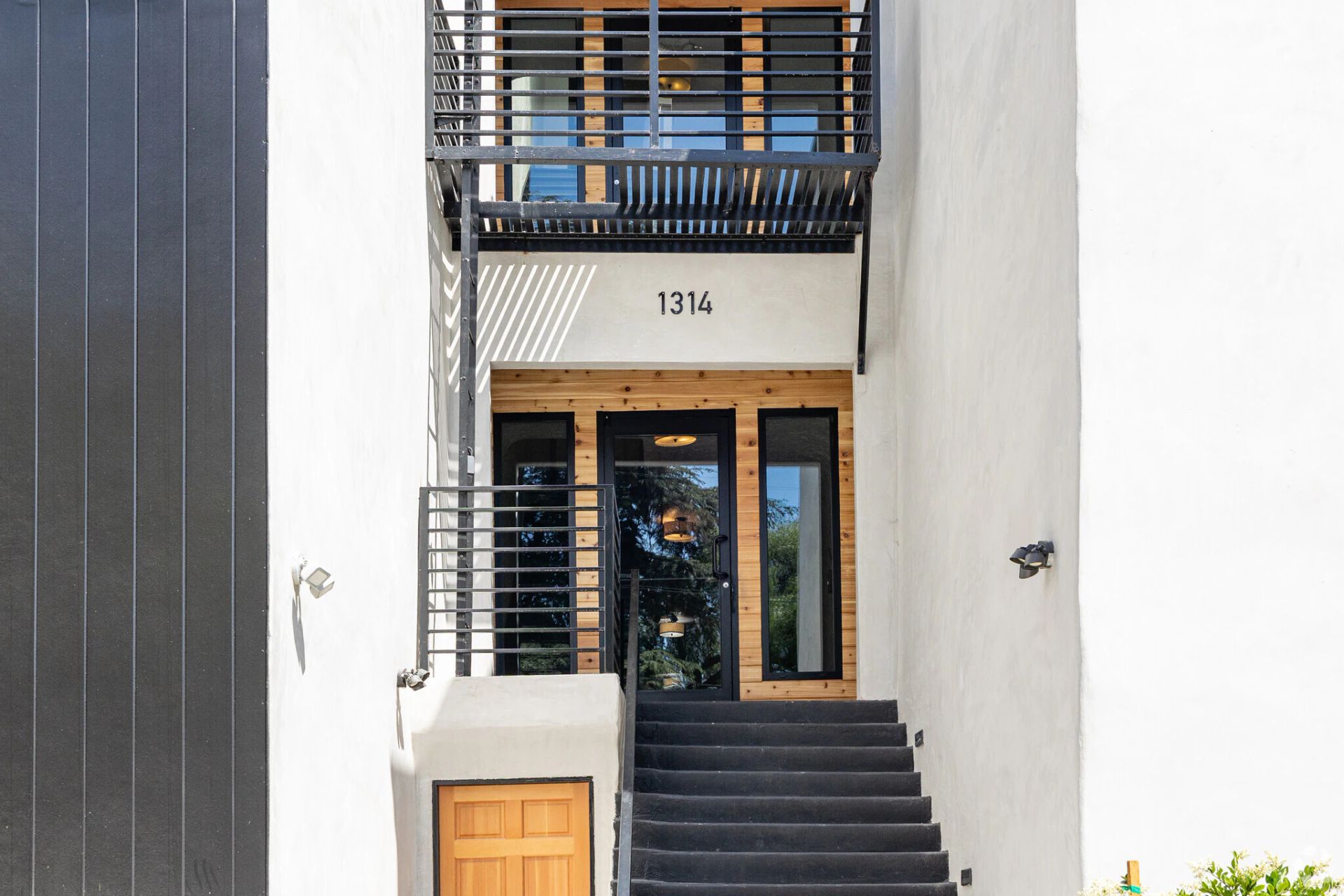 White building entrance with black stairs, metal railing, and wooden door.