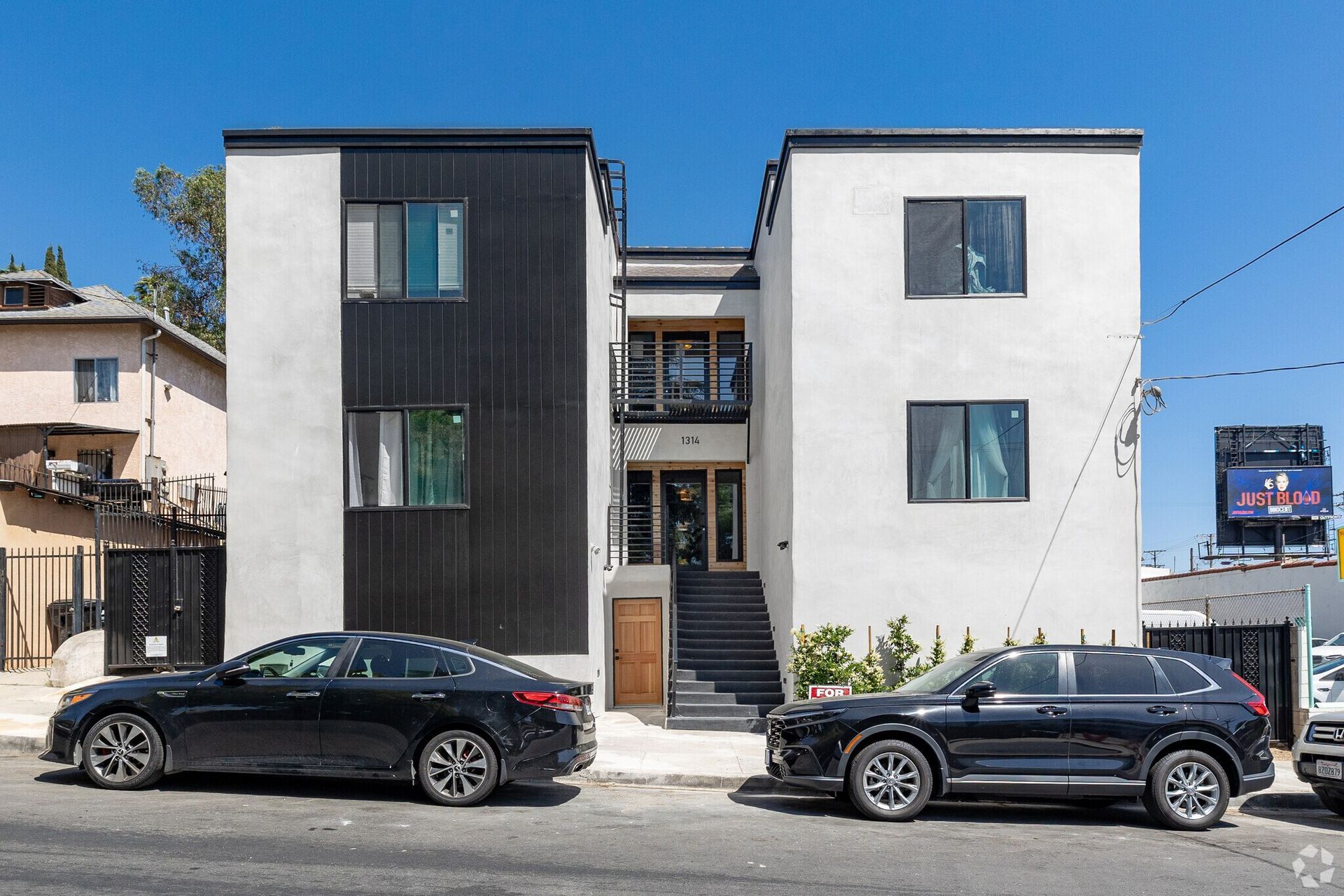 Modern apartment building with black and white facade; cars parked on street.