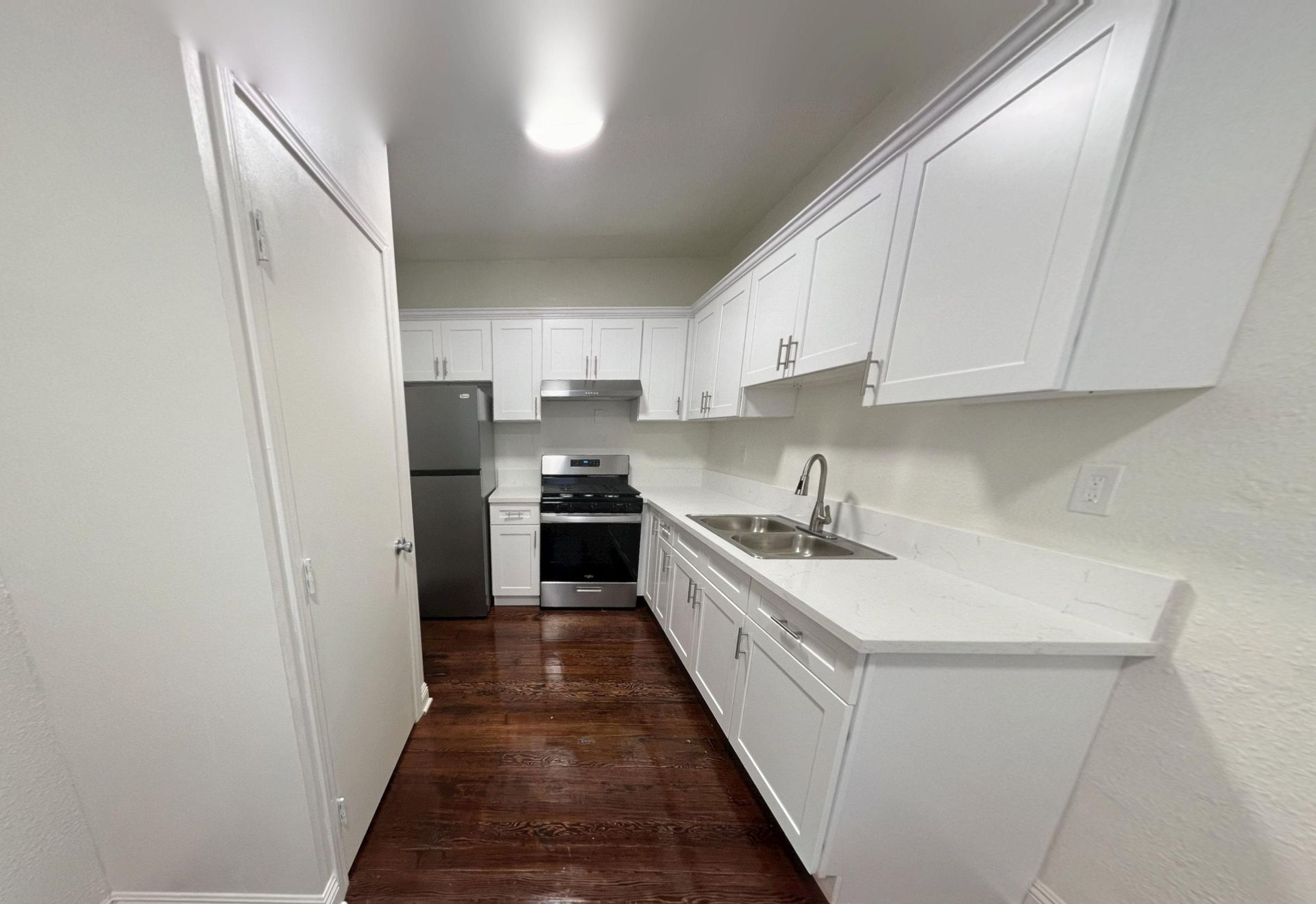 Kitchen with white cabinets, stainless steel appliances, and dark wooden floors.