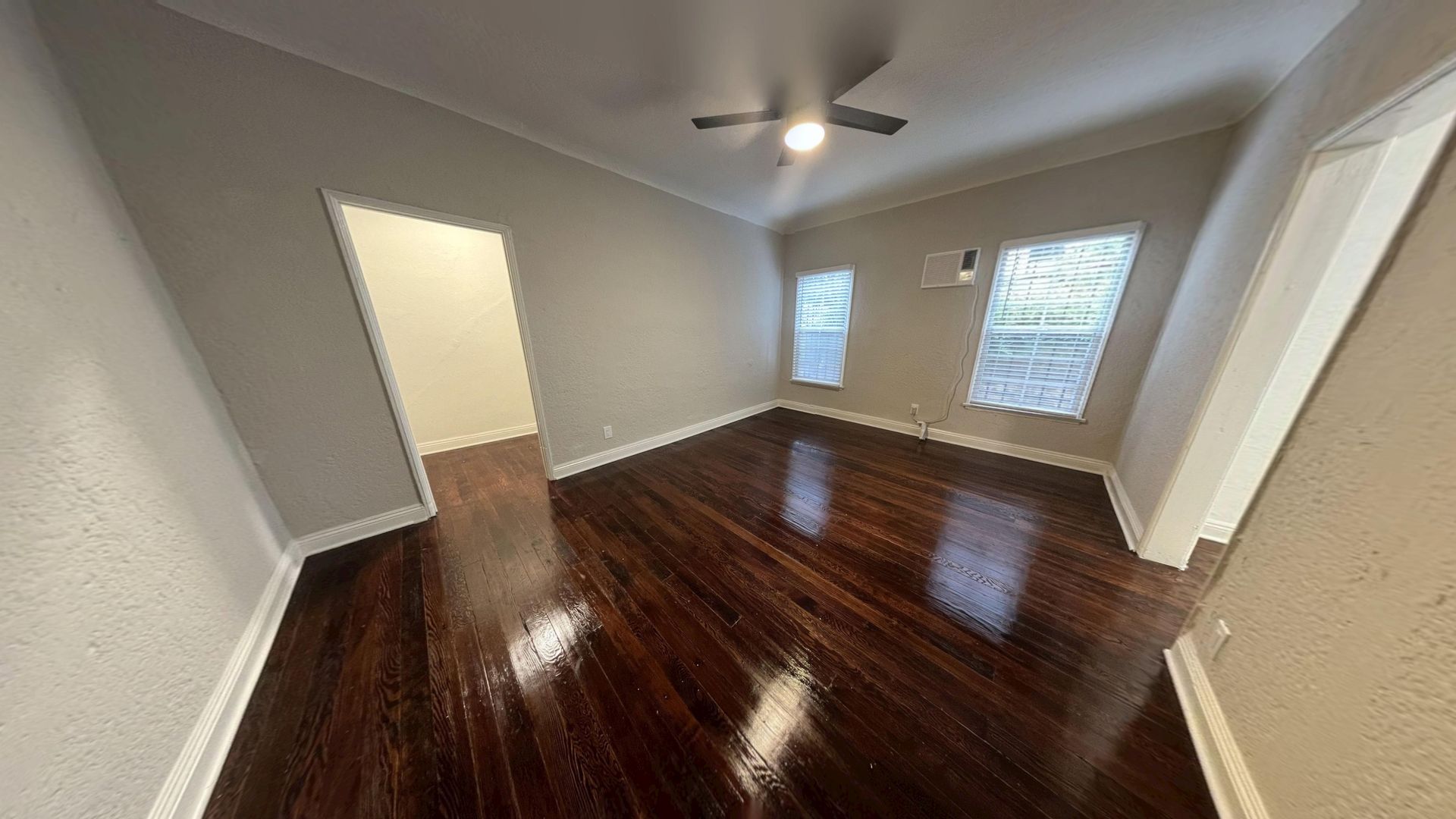 Empty room with dark wood floors, two windows, and an open doorway. Gray walls and white trim.