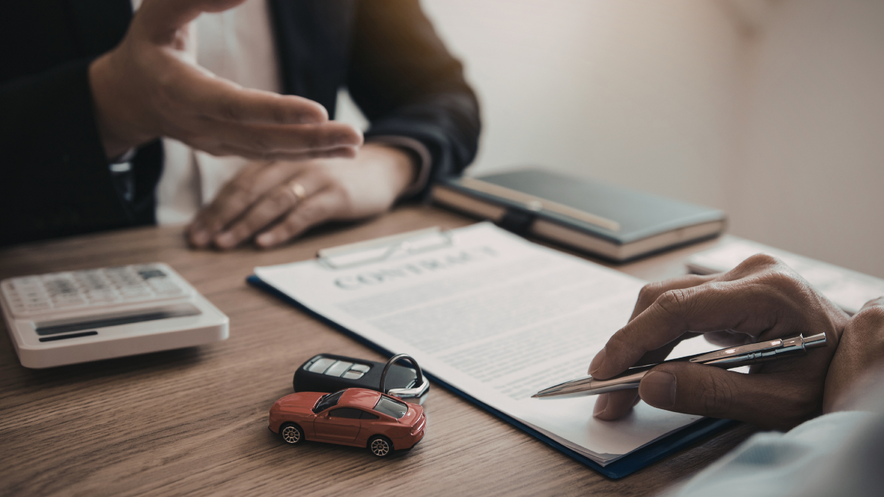 Two people review a contract on a wooden table, with a calculator and small toy car nearby.