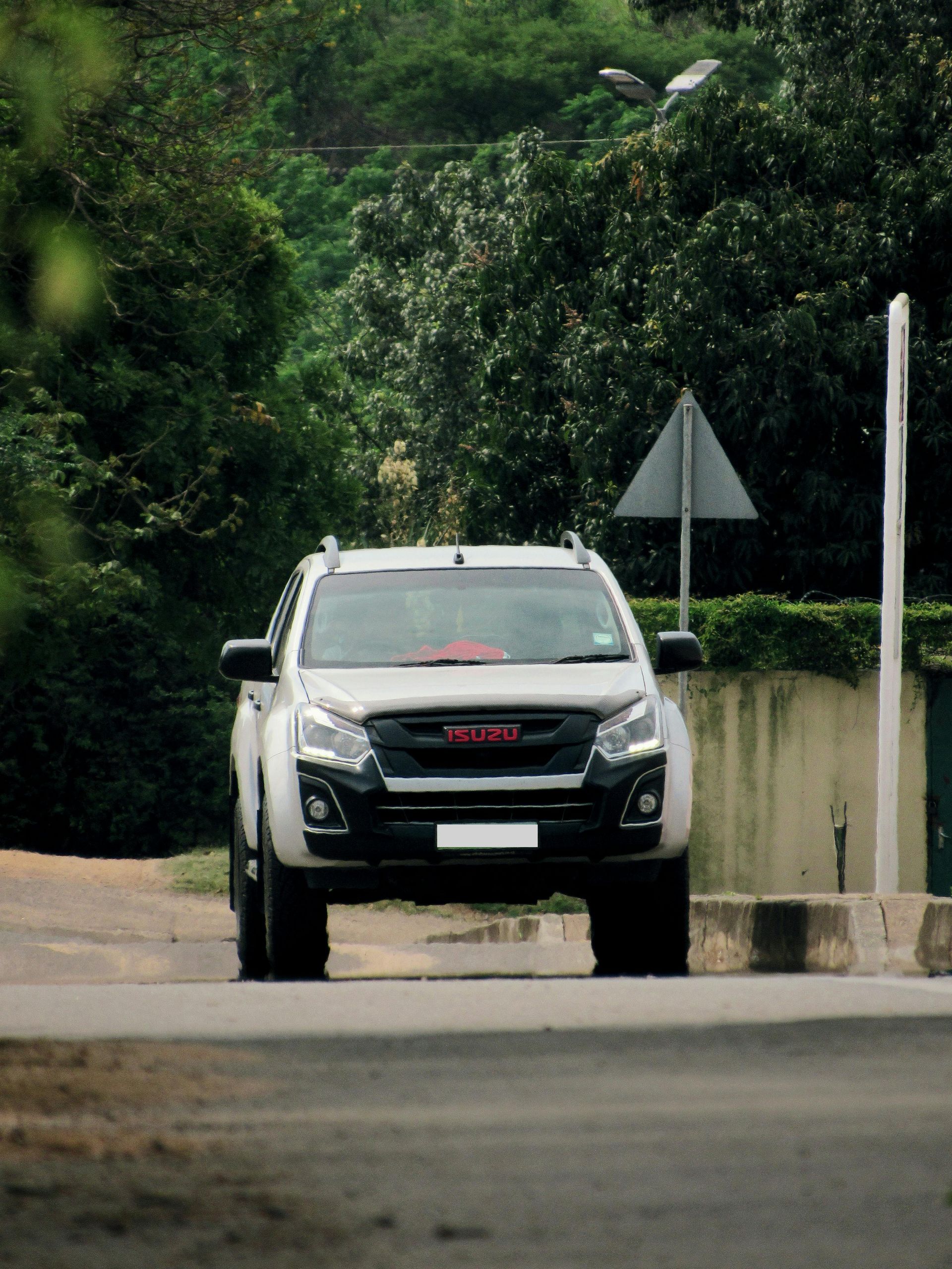 White Isuzu SUV on a road, with green trees in the background. A road sign is visible to the right.