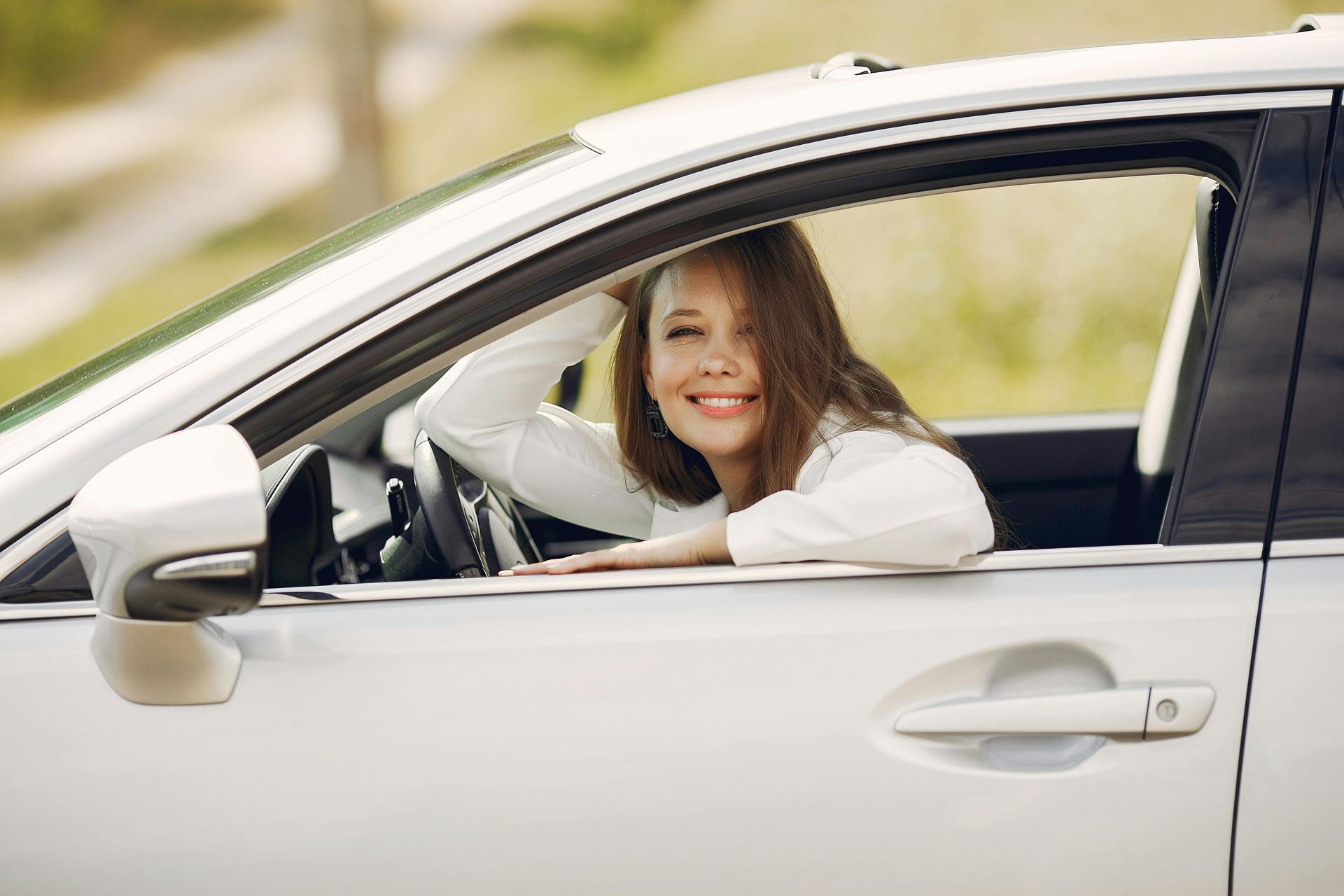 Woman smiling from the driver’s seat of a white car with the window down