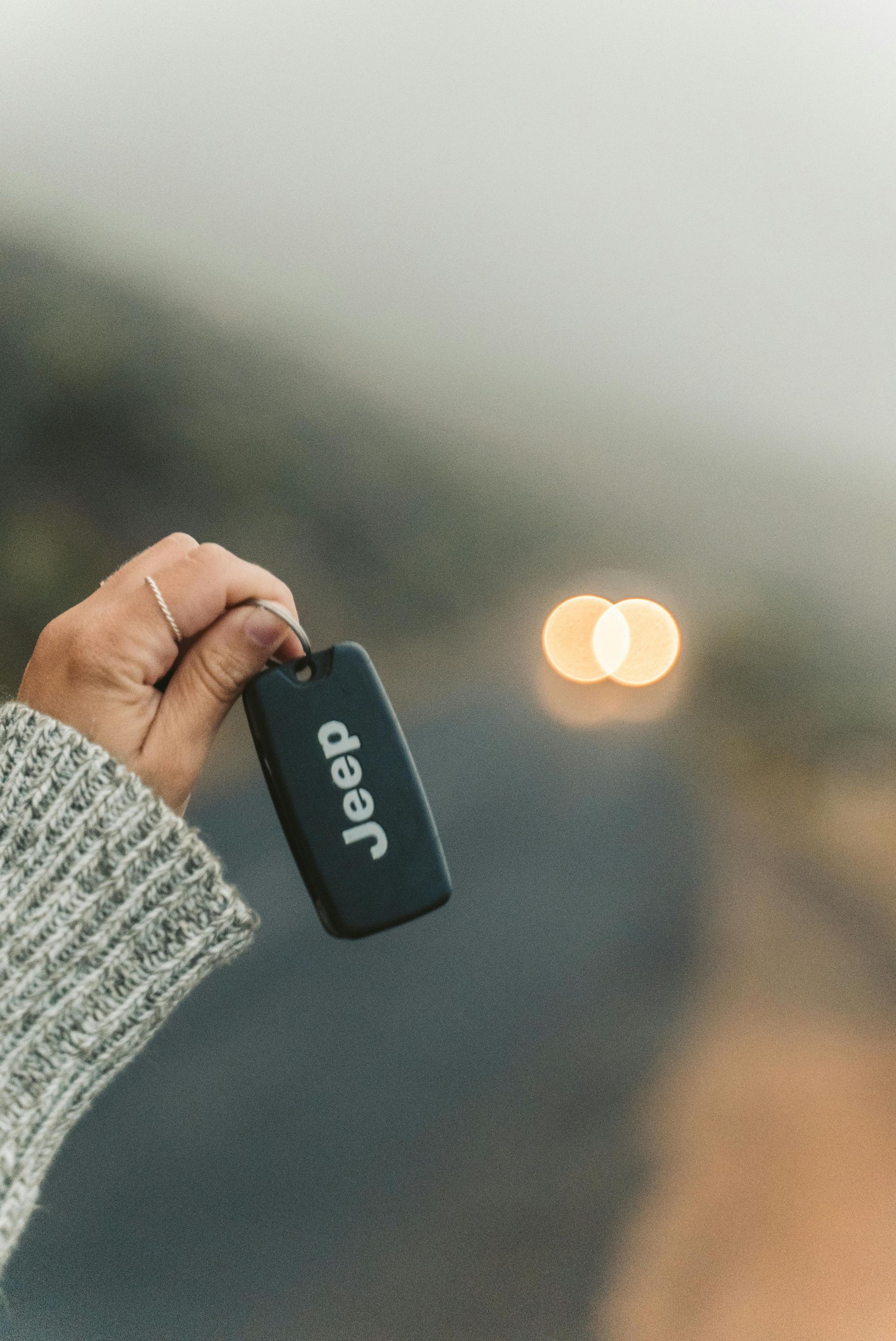 Hand holding a black Jeep key fob with blurred car headlights in the background