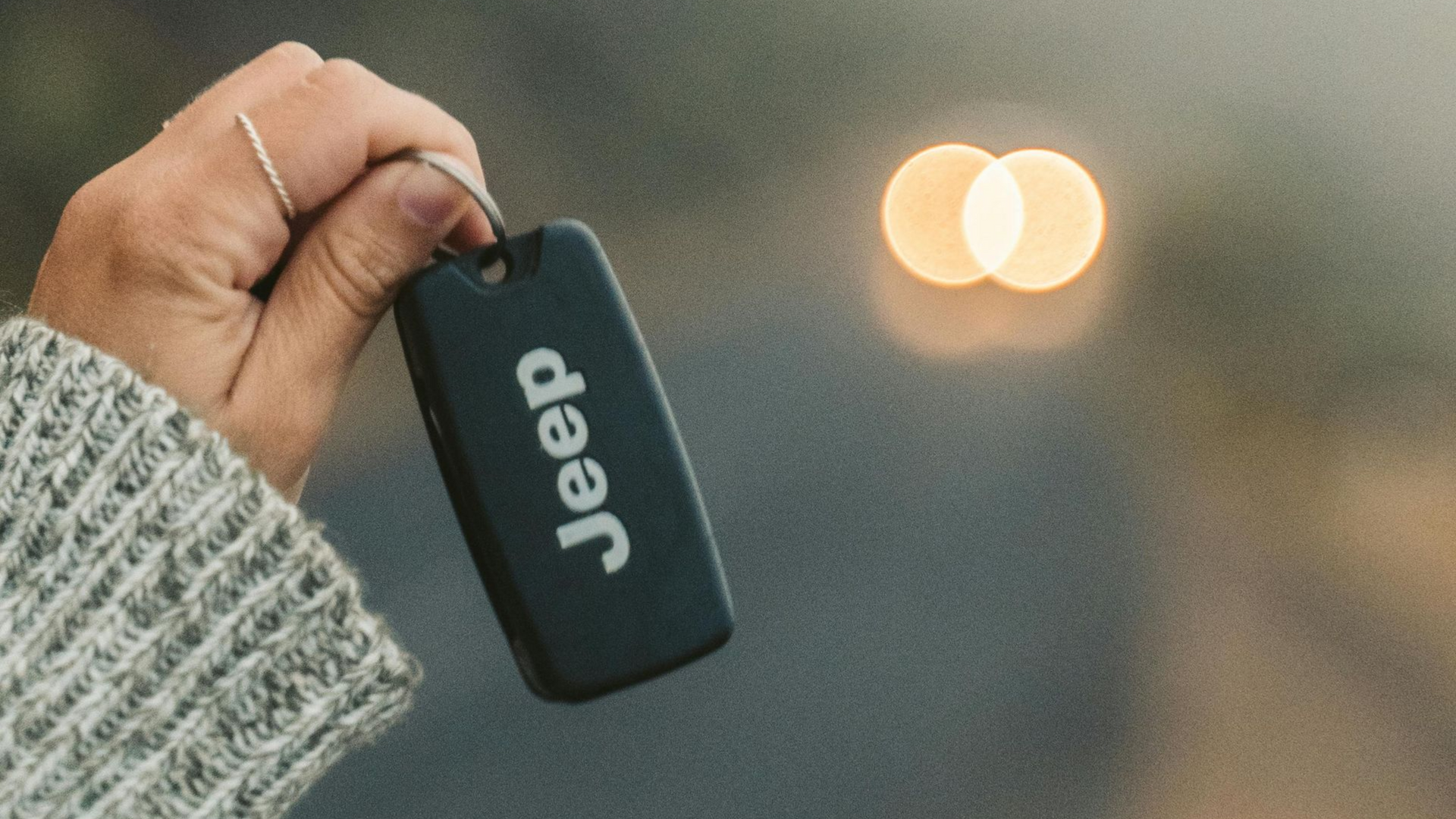 Hand holding a black Jeep key fob with blurred headlights in the background