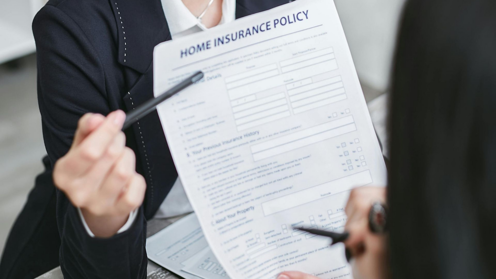 Two people in professional attire review a home insurance policy document, with one person pointing to the text.