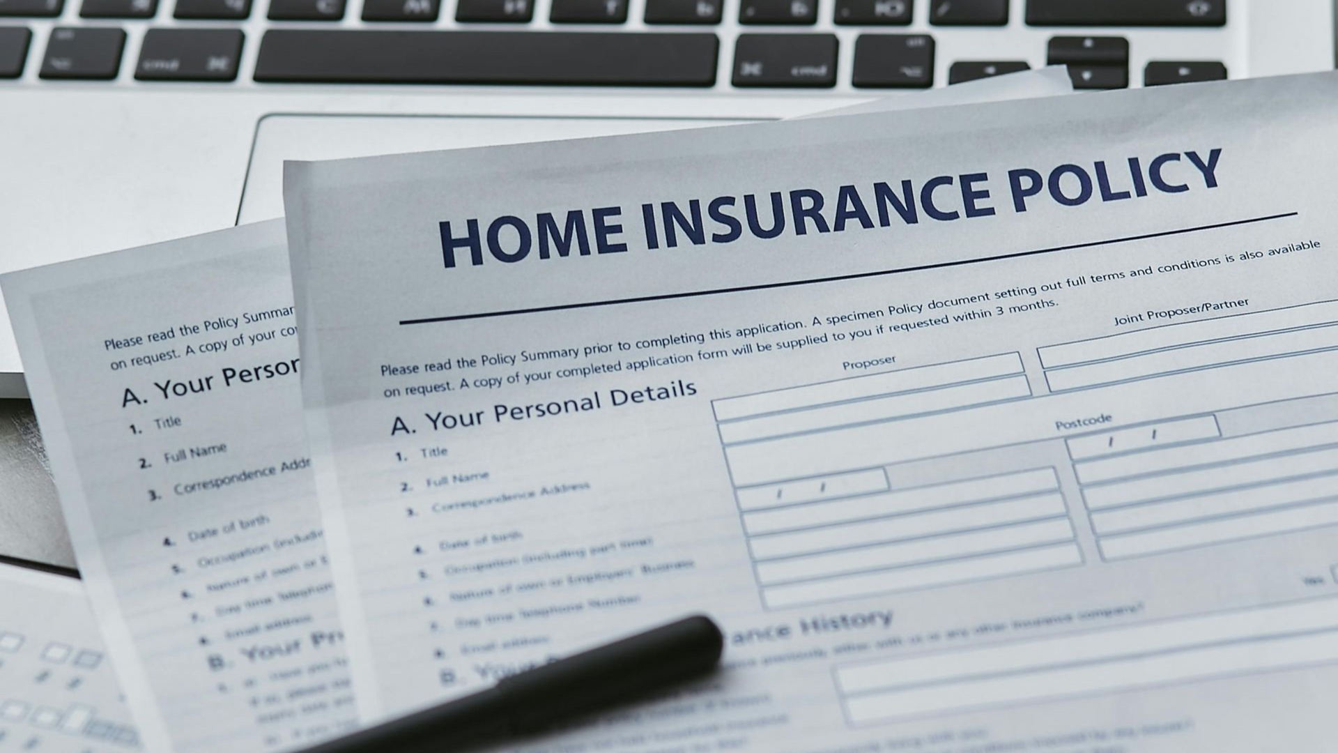 A home insurance policy form lies on a desk next to a pen and a laptop keyboard.