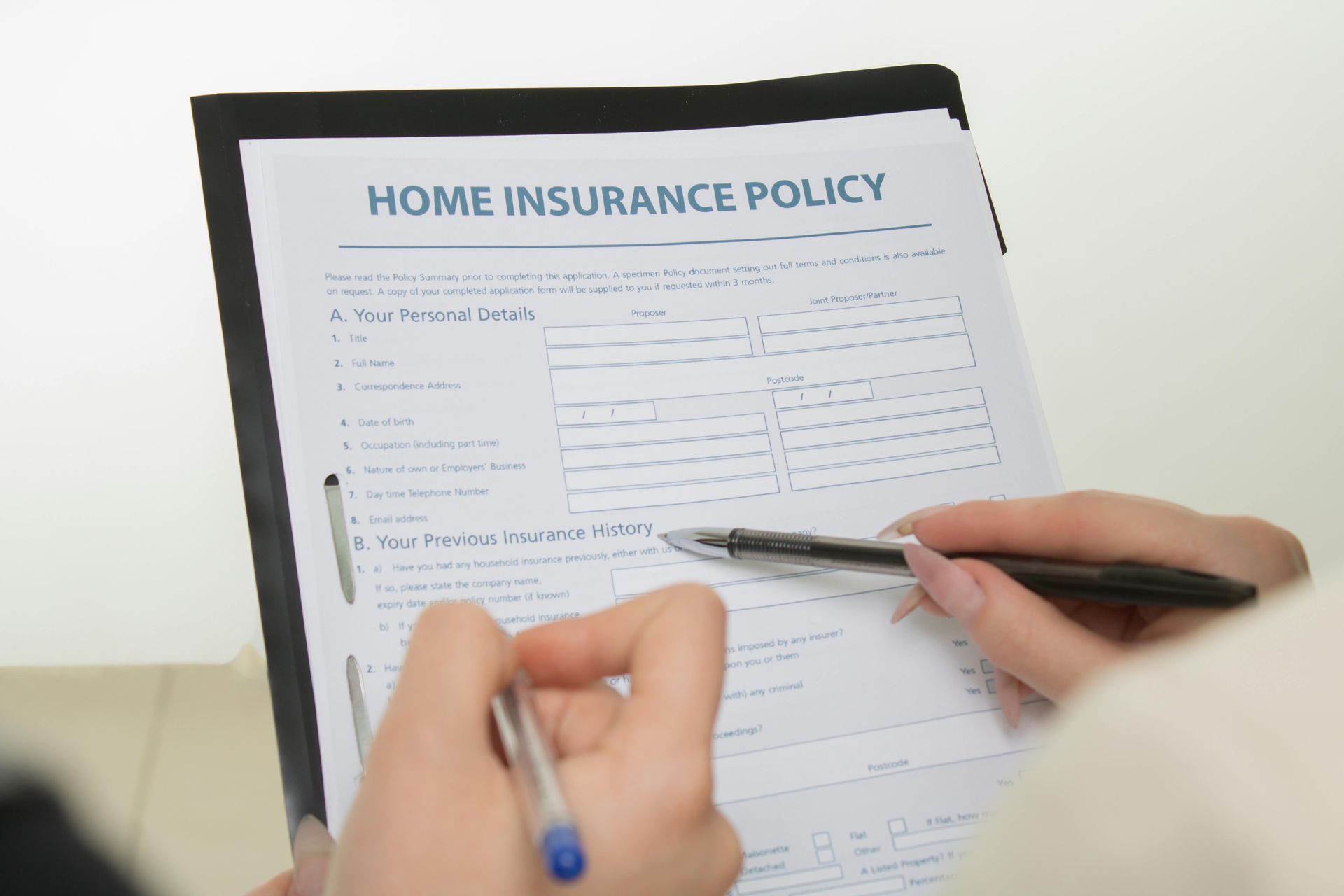 Close-up view of hands holding pens while reviewing a home insurance policy form on a clipboard.