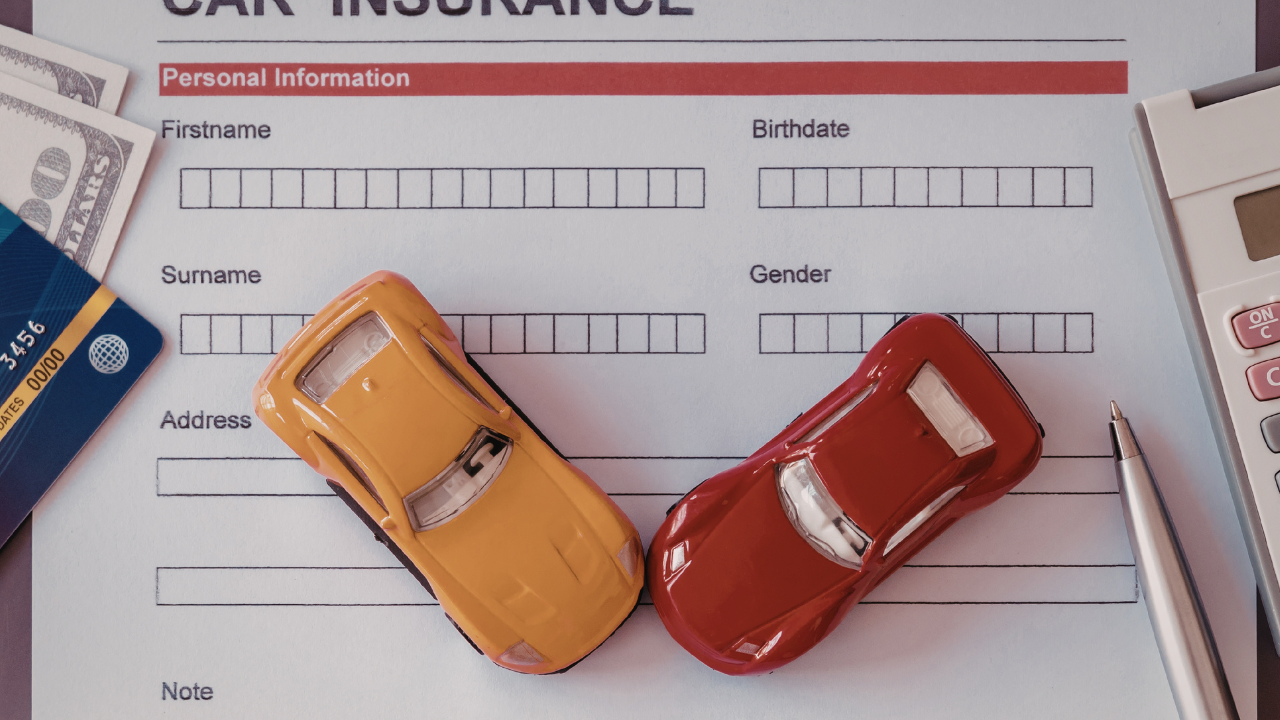 A car insurance form with a toy yellow car, toy red car, pen, calculator, bank card, and cash resting on top.