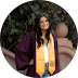 Woman in graduation gown with gold sash, smiling, outdoors.