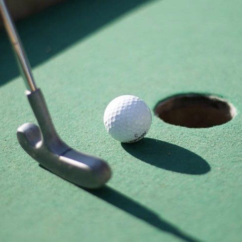 Minigolfboll nära hålet, putter bredvid, på en greenbana.