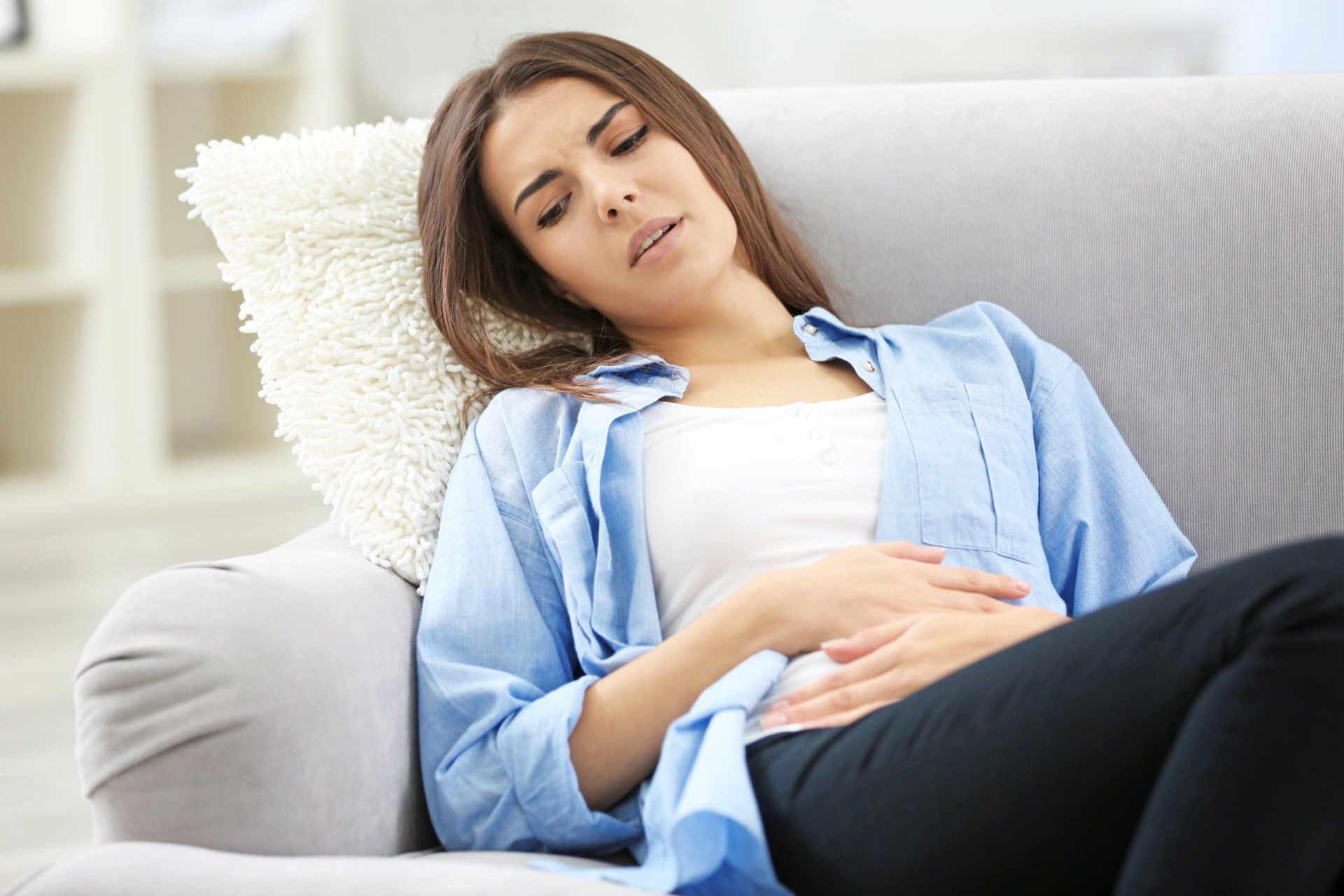 Uma mulher está deitada no sofá com as mãos na barriga.