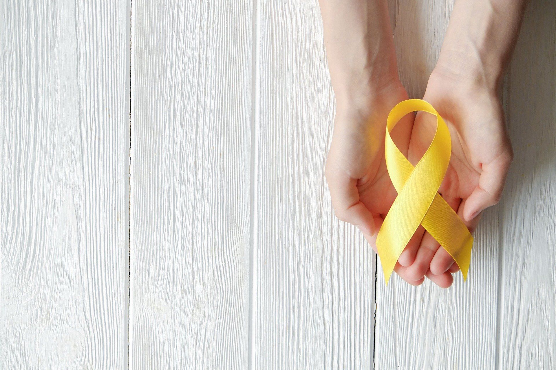 Uma pessoa está segurando uma fita amarela nas mãos sobre uma mesa de madeira branca.