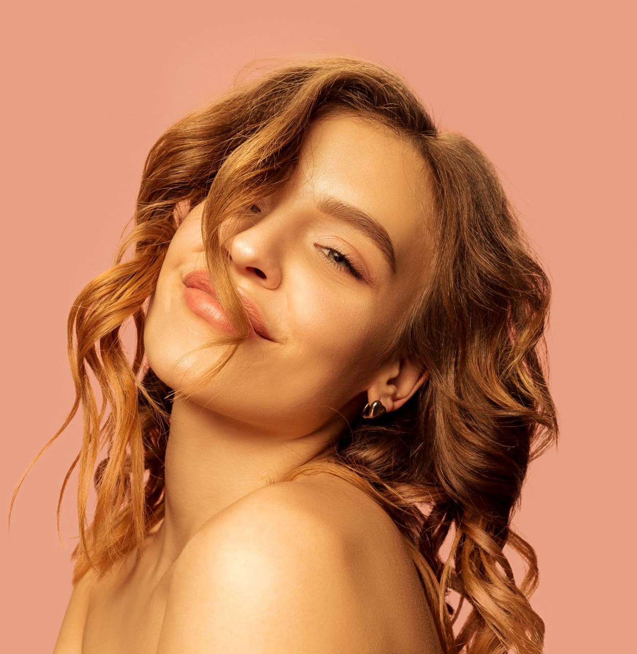 Uma mulher com cabelos cacheados está sorrindo e olhando para a câmera em um fundo rosa.