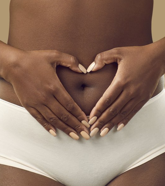 Uma mulher está fazendo um formato de coração com as mãos na barriga.