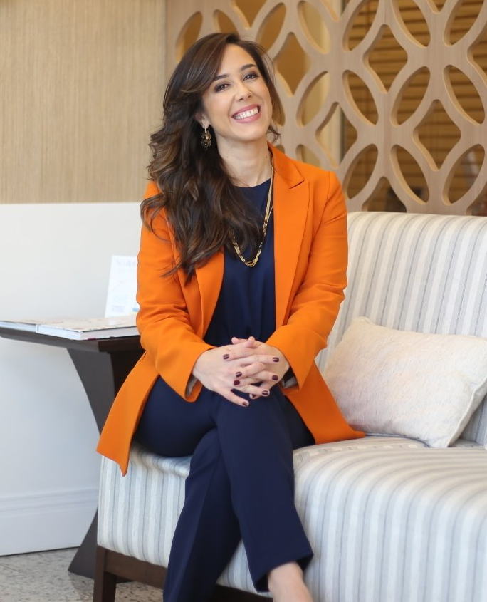 Uma mulher com uma jaqueta laranja está sentada em um sofá