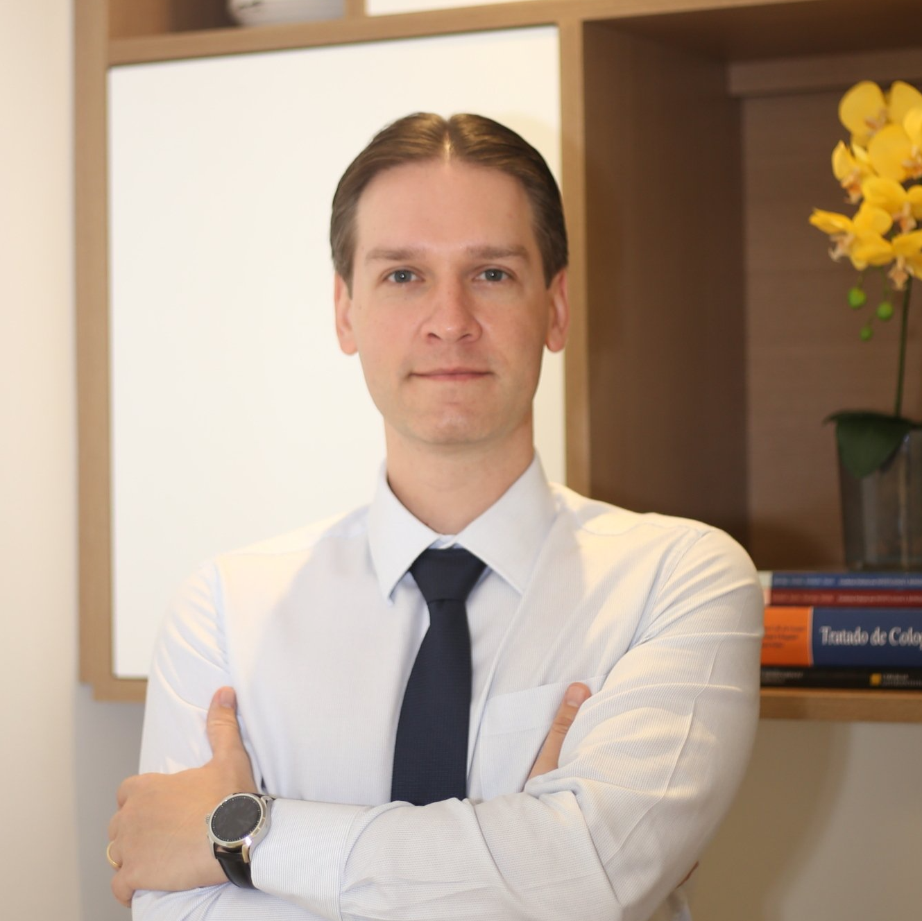 Um homem de camisa branca e gravata está de braços cruzados