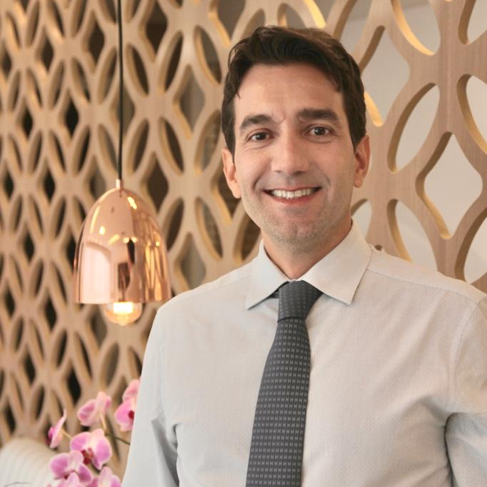 Um homem de camisa branca e gravata sorri para a câmera