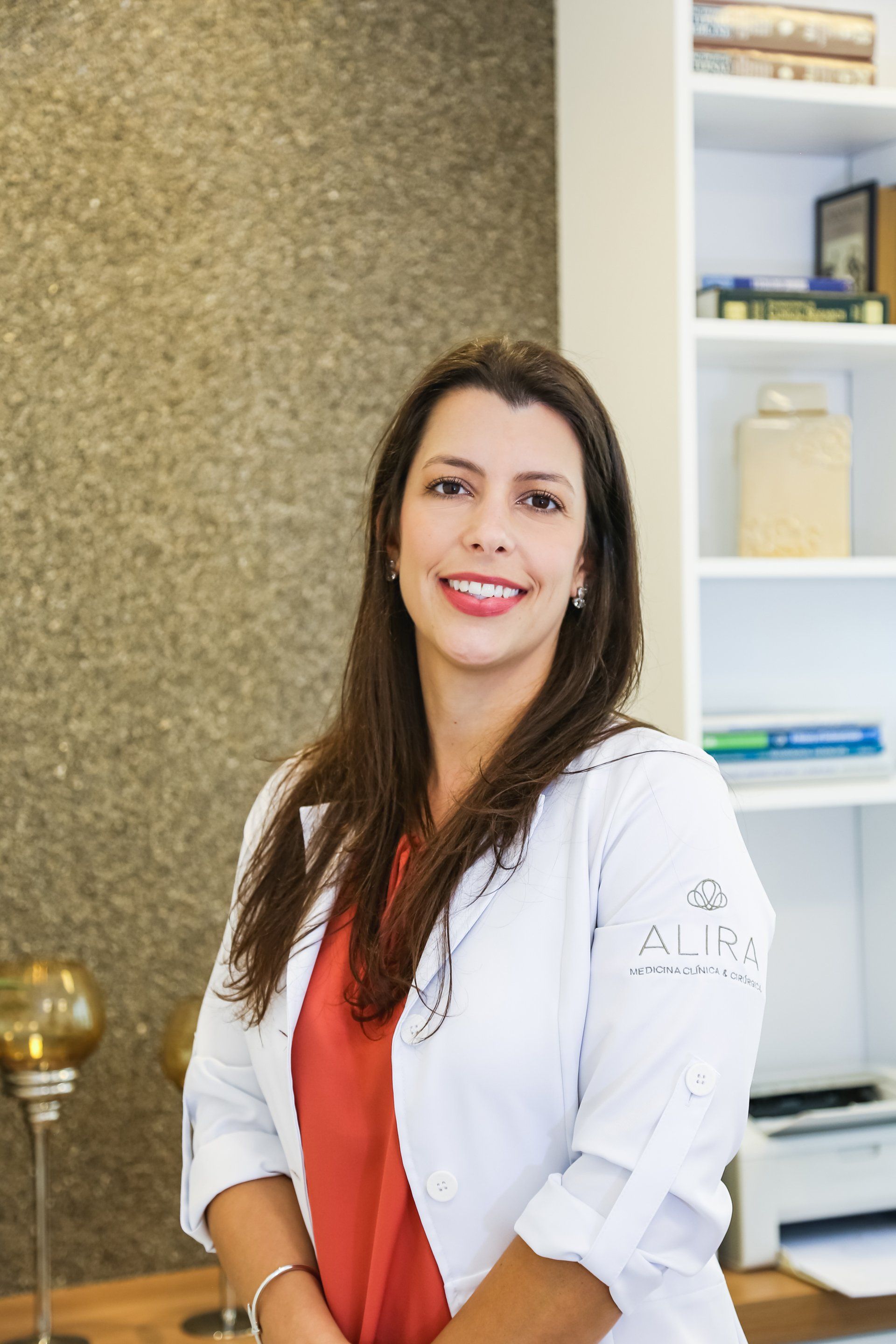 Uma mulher de jaleco está parada em frente a uma estante de livros.