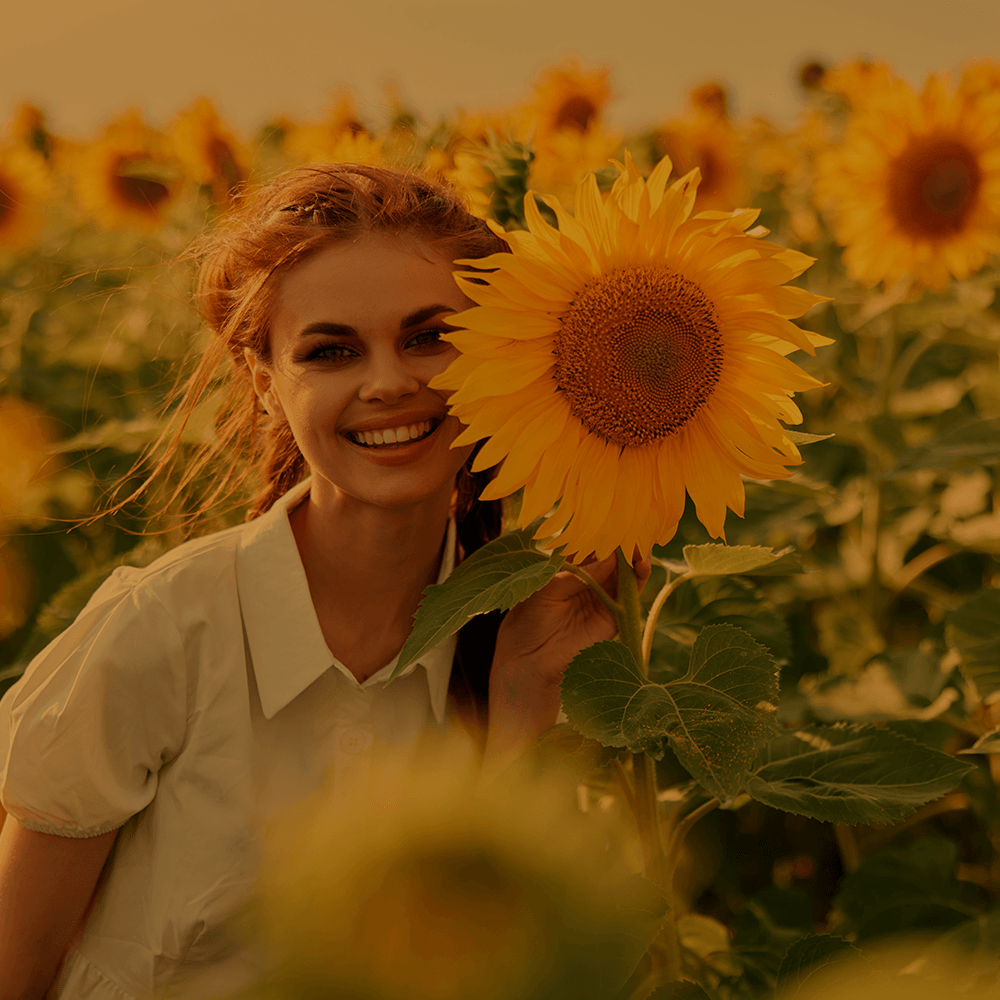 Uma mulher está segurando um girassol na frente do rosto em um campo de girassóis.