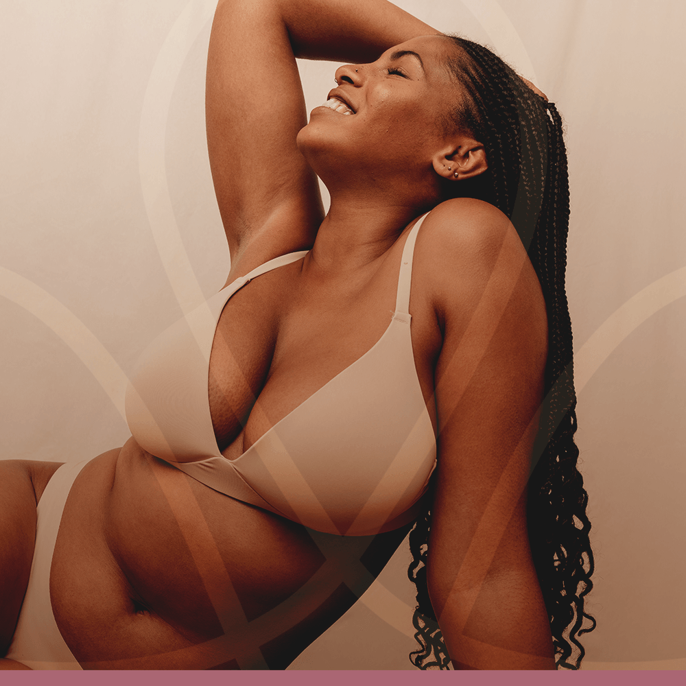 Uma mulher de sutiã está deitada com a cabeça apoiada nas mãos e sorrindo.